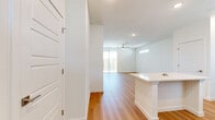 This two-story home in Hutto, Texas offers a thoughtfully designed layout across two floors. The main level is anchored by an open-concept kitchen and living area, bathed in natural light from large windows and sliding glass doors. The kitchen is a standout feature, showcasing a two-tone design with crisp white upper cabinetry and bold navy lower cabinets, complemented by a classic tile backsplash, white quartz countertops, a large center island, and a full suite of stainless steel appliances. Warm-toned hardwood flooring flows throughout the main level, enhancing the bright, airy atmosphere created by recessed lighting and a ceiling fan in the living area. Upstairs, the three bedrooms are finished with plush carpeting and feature windows that bring in natural light. The spacious primary bedroom connects to an en-suite bathroom with hardwood floors, a navy vanity with white quartz countertops, a large mirror, and access to a dedicated walk-in closet. The second bathroom mirrors the home's modern aesthetic, featuring a tiled tub-surround, matching navy cabinetry, and hardwood flooring. Clean white walls and panel-style doors carry a cohesive, contemporary style throughout the entire home.