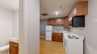 Located at 301 W 1st St in downtown Duluth, Minnesota, this thoughtfully laid-out unit makes excellent use of its compact footprint. The open-plan main area seamlessly combines the living, dining, and kitchen spaces into one cohesive room, creating a flexible and functional environment. Warm-toned hardwood flooring runs throughout the main living area, lending a sense of continuity and warmth to the space. Large, dark-framed windows in the living area allow natural light to filter in while offering views of the surrounding urban streetscape, complemented by a classic cast-iron radiator that speaks to the building's character.

The kitchen is well-appointed with warm wood cabinetry, upper and lower storage, a full-size refrigerator, electric range, sink, and an over-the-range microwave. Notably, the kitchen area also accommodates an in-unit washer and dryer, adding a layer of everyday convenience. The drop ceiling in the kitchen area contrasts with the more traditional feel of the living space. The bathroom features clean white walls, neutral tile flooring, a wood-vanity with storage, and accessible grab bars. Two closets provide additional storage throughout the unit, keeping the living areas uncluttered and organized.