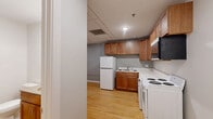 Located at 301 W 1st St in downtown Duluth, Minnesota, this thoughtfully laid-out unit makes excellent use of its compact footprint. The open-plan main area seamlessly combines the living, dining, and kitchen spaces into one cohesive room, creating a flexible and functional environment. Warm-toned hardwood flooring runs throughout the main living area, lending a sense of continuity and warmth to the space. Large, dark-framed windows in the living area allow natural light to filter in while offering views of the surrounding urban streetscape, complemented by a classic cast-iron radiator that speaks to the building's character.

The kitchen is well-appointed with warm wood cabinetry, upper and lower storage, a full-size refrigerator, electric range, sink, and an over-the-range microwave. Notably, the kitchen area also accommodates an in-unit washer and dryer, adding a layer of everyday convenience. The drop ceiling in the kitchen area contrasts with the more traditional feel of the living space. The bathroom features clean white walls, neutral tile flooring, a wood-vanity with storage, and accessible grab bars. Two closets provide additional storage throughout the unit, keeping the living areas uncluttered and organized.