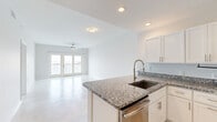 Located at 1400 Bayou Shore Dr in Galveston, Texas, this single-story, 3-bedroom, 2-bathroom home offers a clean, modern design throughout. Light-toned tile flooring runs through the main living areas, creating a bright and cohesive feel as you move from the entry hallway into the open-concept kitchen and living room. The kitchen is well-appointed with white shaker-style cabinetry, granite countertops, a central island with an undermount sink and pull-down faucet, and a full suite of stainless steel appliances including a refrigerator, range, microwave, and dishwasher. The adjacent living room is bathed in natural light from a set of glass doors leading to a balcony, and is equipped with a ceiling fan. The three bedrooms feature soft carpeting and ceiling fans, with the spacious primary bedroom offering comfortable proportions. Both bathrooms include granite-topped vanities and tub-shower combinations. A dedicated laundry room houses a full-size Maytag washer and dryer with upper cabinetry for additional storage. The overall aesthetic is bright, neutral, and move-in ready, reflecting a contemporary coastal sensibility suited to the Galveston setting.