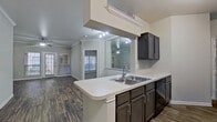 This single-story unit offers a well-designed open-concept layout connecting the kitchen and living area. The kitchen is equipped with dark espresso cabinetry, light countertops, stainless steel appliances including a refrigerator, electric range, and built-in microwave, along with a peninsula with a double sink that faces the living space. A large mirrored wall in the kitchen area enhances the sense of depth and reflects natural light. The living area features crown molding, a ceiling fan, and dark wood-style flooring, with glass doors providing outdoor access and allowing natural light to fill the space.

The bedrooms are carpeted and finished with crown molding and ceiling fans. One bedroom features angled walls and corner windows, adding architectural interest. The primary bathroom includes a dual-sink vanity with dark cabinetry, a large mirror, and wood-style flooring. A second bathroom offers a single-sink vanity with a tub-shower combination. A dedicated in-unit laundry area accommodates a full-size washer and dryer side by side. Neutral tones and consistent finishes throughout give the space a cohesive, functional character.