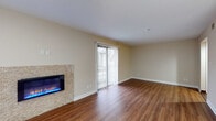 This single-floor space is thoughtfully designed to maximize both comfort and functionality. The living area serves as the focal point of the unit, showcasing rich hardwood-style flooring that runs throughout and a striking stone-surround electric fireplace that adds warmth and visual interest to the room. A large sliding glass door fitted with vertical blinds allows an abundance of natural light to flood the space while providing convenient outdoor access. The neutral, warm-toned walls and textured ceiling complement the overall aesthetic.

The kitchen is well-appointed with dark espresso cabinetry featuring frosted glass upper panels and sleek hardware. Light countertops provide a clean contrast, while a decorative tile backsplash adds a refined touch. Stainless steel appliances, including a refrigerator, dishwasher, and microwave, complete the modern look.

The bathroom continues the cohesive design language with wood-look tile flooring, a floating vanity topped with a light countertop, and a backlit mirror that adds a contemporary feel. An adjacent walk-in closet offers practical storage. The overall ambiance of the space is clean, modern, and move-in ready.