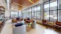 Located at 1308 Roseneath Rd in Richmond, Virginia, this single-floor amenity space combines industrial architecture with contemporary design to create a dynamic, multi-functional environment. The space is defined by its striking wood-slat ceilings with integrated lighting, exposed metal ductwork, and expansive floor-to-ceiling steel-framed windows that flood the interior with natural light and provide open views of the surrounding neighborhood.

The lounge area serves as the centerpiece of the space, furnished with cognac leather sofas, modern accent chairs, and a woven rattan side table, all arranged atop layered area rugs over polished concrete floors. This welcoming seating arrangement transitions seamlessly into a recreation zone, where a full-size pool table, wall-mounted television, and open shelving units create an engaging social atmosphere. Vintage-style Coca-Cola artwork and bold typographic prints add personality and visual interest throughout.

A dedicated dining and collaborative work area features sleek black tables paired with warm-toned chairs, positioned directly beside the glass window walls for an airy, light-filled setting. The kitchenette is equipped with stainless steel countertops, dark tile backsplash, a sink, dishwasher, and refrigeration, providing full functionality for gatherings and events. Together, these zones create a cohesive, well-appointed communal space.