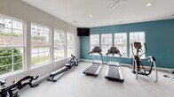 Located at 180 Embassy Dr in Fort Mill, SC, this single-floor fitness center is thoughtfully designed to support a wide range of workout routines. The space is divided into distinct functional zones, each tailored to a specific type of exercise. The cardio area is lined with large windows that flood the room with natural light and offer views of the surrounding community, creating an open and energizing atmosphere. It is equipped with treadmills, a rowing machine, and an elliptical, complemented by a wall-mounted television and a ceiling fan for comfort. An adjacent strength training zone features a full rack of dumbbells, adjustable workout benches, and a large wall mirror that enhances the sense of space while allowing users to monitor their form. A teal accent wall adds a bold, motivating visual element to this section. A separate area is dedicated to functional and combat training, housing a cable machine system, a heavy punching bag, a multi-tier rack with medicine balls and accessories, and an inspiring motivational wall mural. Recessed lighting and ceiling fans throughout ensure a comfortable environment year-round. The space is accessible via a glass-panel door and finished with durable, easy-to-maintain flooring suited for high-traffic athletic use.