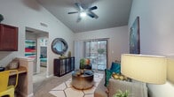 This single-story residence is thoughtfully laid out to maximize comfort and functionality across its key living spaces. The living room serves as the heart of the home, distinguished by soaring vaulted ceilings and a ceiling fan that enhance the sense of openness. Soft carpeting underfoot and a large sliding glass door fitted with vertical blinds invite natural light while providing direct access to an outdoor patio with views of the surrounding area. The space comfortably accommodates a seating arrangement centered around a stylish coffee table.

The galley-style kitchen features rich dark cabinetry, light granite-style countertops, hardwood flooring, and a full suite of black appliances including a refrigerator, range, microwave, and dishwasher. A doorway from the kitchen leads directly to the dedicated laundry room, which houses a full-size washer and dryer with shelving above.

The bedroom offers carpeted flooring, a ceiling fan, a standard window with blinds and curtain panels, and a closet. The full bathroom is outfitted with dark wood cabinetry, granite-style countertops, a combined tub and shower, and hardwood flooring, completing this well-appointed residence.