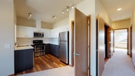Located at 1688 Stella Avenue in Wenatchee, Washington, this single-floor residence offers a well-designed layout with modern finishes throughout. The kitchen is a standout feature, showcasing a two-tone design with dark lower cabinetry and crisp white upper cabinets, complemented by stainless steel appliances including a refrigerator, range, and built-in microwave. Light wood-look flooring, white quartz countertops, a peninsula, and track lighting complete the kitchen's contemporary aesthetic. The spacious living area is finished with neutral carpet and features large windows that allow generous natural light and views of the surrounding neighborhood and distant mountain scenery. Bedrooms are carpeted for comfort and include closets with built-in rods for ample storage. Warm wood-tone doors and trim provide a consistent design accent throughout the unit. Two bathrooms are present: one full bath featuring a shower/tub combination with sliding glass doors, a white vanity, and wood-look flooring, and a second bathroom with a similar vanity and flooring style. An in-unit laundry area is also visible in the floor plan. The overall ambiance is clean, modern, and functional, making this a well-equipped residence in the Wenatchee area.