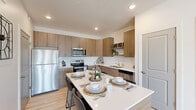 This well-appointed single-floor residence showcases a thoughtful layout and contemporary design throughout. The open-concept kitchen is a standout feature, outfitted with warm wood-tone cabinetry, stainless steel appliances, a classic white subway tile backsplash, and a generously sized island with a quartz countertop that comfortably seats multiple guests — ideal for both meal prep and casual dining. Light wood-style flooring flows seamlessly through the main living areas, complementing the neutral color palette and enhancing the sense of openness.

The living room is bright and inviting, benefiting from large windows and a glass-panel door that flood the space with natural light and provide views to the outdoors. A ceiling fan adds a practical and stylish touch to the room's relaxed ambiance. An additional flex room offers versatile living space, currently styled as a sitting lounge. The bathroom features matching wood-tone vanity cabinetry, white quartz countertops, and light hardwood-style flooring, maintaining the cohesive modern aesthetic found throughout the home. A dedicated in-unit laundry area houses a full-sized washer and dryer with overhead shelving for added storage convenience.