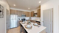 This well-appointed single-floor residence showcases a thoughtful layout and contemporary design throughout. The open-concept kitchen is a standout feature, outfitted with warm wood-tone cabinetry, stainless steel appliances, a classic white subway tile backsplash, and a generously sized island with a quartz countertop that comfortably seats multiple guests — ideal for both meal prep and casual dining. Light wood-style flooring flows seamlessly through the main living areas, complementing the neutral color palette and enhancing the sense of openness.

The living room is bright and inviting, benefiting from large windows and a glass-panel door that flood the space with natural light and provide views to the outdoors. A ceiling fan adds a practical and stylish touch to the room's relaxed ambiance. An additional flex room offers versatile living space, currently styled as a sitting lounge. The bathroom features matching wood-tone vanity cabinetry, white quartz countertops, and light hardwood-style flooring, maintaining the cohesive modern aesthetic found throughout the home. A dedicated in-unit laundry area houses a full-sized washer and dryer with overhead shelving for added storage convenience.