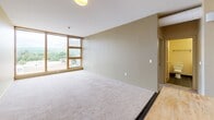 Located at 120 E Green St in downtown Ithaca, New York, this single-floor unit offers a well-organized layout with a open living area, kitchen, multiple bedrooms, and two bathrooms. The living area is generously sized, featuring soft carpeting and warm, neutral-toned walls that create a welcoming atmosphere. Large floor-to-ceiling windows and horizontal band windows frame sweeping views of Ithaca's surrounding hills and cityscape, filling the space with natural light.

The kitchen is efficiently designed in a U-shaped configuration, equipped with white cabinetry, dark countertops, a white electric range, and dark speckled flooring. A breakfast bar connects the kitchen to the living area, enhancing the open-concept feel. Exposed ductwork adds an industrial touch to the overall design.

The bedrooms continue the warm color palette with carpeted floors and horizontal band windows that offer scenic views of the treeline and surrounding neighborhood. Both bathrooms are finished with dark tile flooring and dark-base vanities topped with white countertops. One bathroom features a walk-in shower, while the other includes a soaking tub with a shower curtain, both appointed with well-lit mirrors above the sinks.