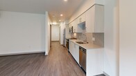 Located at 110 Roy St in Seattle's Lower Queen Anne neighborhood, this thoughtfully designed studio unit offers a clean, modern aesthetic across its single floor. Wood-look plank flooring runs continuously throughout the space, providing visual cohesion and warmth.

The open-plan kitchen and living area form the heart of the unit. The kitchen is efficiently laid out with white flat-front cabinetry extending to the ceiling, light-toned countertops, a tile backsplash, and a full suite of stainless steel appliances including a range, microwave, refrigerator, and dishwasher. A hallway connects the kitchen area to the remaining rooms, keeping the layout organized despite the compact footprint. The living area benefits from large windows and a glass door that invite natural light and offer views of the outdoor surroundings. A wall-mounted mini-split unit provides climate control.

The bathroom is finished in a contemporary style, featuring a tiled tub-and-shower combination, a single vanity with an undermount sink, a large mirror, and wood-look flooring consistent with the rest of the unit. A dedicated closet provides additional storage. Recessed lighting throughout the kitchen and hallway areas enhances the overall brightness, contributing to an efficient, modern living environment.