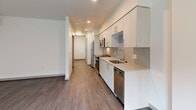 Located at 110 Roy St in Seattle's Lower Queen Anne neighborhood, this thoughtfully designed studio unit offers a clean, modern aesthetic across its single floor. Wood-look plank flooring runs continuously throughout the space, providing visual cohesion and warmth.

The open-plan kitchen and living area form the heart of the unit. The kitchen is efficiently laid out with white flat-front cabinetry extending to the ceiling, light-toned countertops, a tile backsplash, and a full suite of stainless steel appliances including a range, microwave, refrigerator, and dishwasher. A hallway connects the kitchen area to the remaining rooms, keeping the layout organized despite the compact footprint. The living area benefits from large windows and a glass door that invite natural light and offer views of the outdoor surroundings. A wall-mounted mini-split unit provides climate control.

The bathroom is finished in a contemporary style, featuring a tiled tub-and-shower combination, a single vanity with an undermount sink, a large mirror, and wood-look flooring consistent with the rest of the unit. A dedicated closet provides additional storage. Recessed lighting throughout the kitchen and hallway areas enhances the overall brightness, contributing to an efficient, modern living environment.
