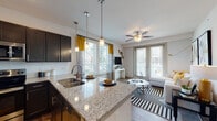 This single-floor residence offers a thoughtfully designed open-concept layout that seamlessly connects the kitchen and living area. The kitchen is equipped with dark espresso cabinetry, stainless steel appliances including a refrigerator, electric range, and over-the-range microwave, all complemented by polished granite countertops and a double-basin sink. Stylish pendant lights hang above the kitchen island, adding a refined touch to the space.

The living area flows naturally from the kitchen and is bathed in natural light from multiple large windows and glass double doors. A ceiling fan enhances comfort, while the open layout creates a welcoming and airy atmosphere with views to the outdoors.

The primary bedroom is a serene retreat featuring plush carpeting, a ceiling fan, and a generously sized window that fills the room with light. It connects to a well-appointed bathroom with matching dark cabinetry, granite countertops, a large mirror, and wood-look flooring. A spacious walk-in closet with built-in shelving and hanging rods provides ample storage.

A second bedroom offers similar comfort with carpeted floors and additional storage. Throughout the residence, consistent use of granite surfaces, dark cabinetry, and wood-look flooring creates a cohesive and modern aesthetic.