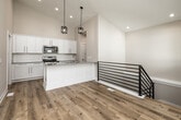This two-story home offers a functional and modern layout across two well-proportioned floors. The main level is anchored by a striking kitchen featuring soaring vaulted ceilings, crisp white shaker cabinetry, a subway tile backsplash, granite countertops, stainless steel appliances, and a central island with an undermount sink and stylish pendant lighting. Light hardwood flooring flows throughout the main level, contributing to a bright, open atmosphere. Adjacent to the kitchen, a dedicated laundry room with stacked washer and dryer adds everyday convenience. The lower level includes a spacious carpeted living area equipped with a ceiling fan and modern stair railing, offering a comfortable secondary gathering space. The home includes four bedrooms, with the primary suite providing a generous footprint and a walk-in closet with wire shelving. Additional bedrooms feature plush carpet and standard closets. Three bathrooms are finished consistently with granite-topped white vanities and brushed nickel hardware; one full bath includes a tub-shower combination. Throughout the home, neutral tones, clean lines, and quality finishes create a cohesive and move-in-ready environment suited for a variety of lifestyles.