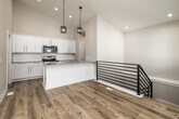 This two-story home offers a functional and modern layout across two well-proportioned floors. The main level is anchored by a striking kitchen featuring soaring vaulted ceilings, crisp white shaker cabinetry, a subway tile backsplash, granite countertops, stainless steel appliances, and a central island with an undermount sink and stylish pendant lighting. Light hardwood flooring flows throughout the main level, contributing to a bright, open atmosphere. Adjacent to the kitchen, a dedicated laundry room with stacked washer and dryer adds everyday convenience. The lower level includes a spacious carpeted living area equipped with a ceiling fan and modern stair railing, offering a comfortable secondary gathering space. The home includes four bedrooms, with the primary suite providing a generous footprint and a walk-in closet with wire shelving. Additional bedrooms feature plush carpet and standard closets. Three bathrooms are finished consistently with granite-topped white vanities and brushed nickel hardware; one full bath includes a tub-shower combination. Throughout the home, neutral tones, clean lines, and quality finishes create a cohesive and move-in-ready environment suited for a variety of lifestyles.