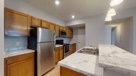 Located at 941 Taylor Station Rd in Gahanna, Ohio, this single-floor unit offers a well-designed layout with a cohesive, modern aesthetic throughout. The kitchen serves as a central highlight, showcasing marble-look countertops, warm honey-toned cabinetry extending to the ceiling, and a full suite of stainless steel appliances including a refrigerator, electric range, and over-the-range microwave. A large island with a built-in sink and pendant lighting above provides additional prep space and casual seating, making it ideal for both cooking and entertaining. Light wood-look flooring runs through the kitchen and living areas, adding warmth and continuity to the space. The bedrooms feature plush carpeting and are generously sized, each with natural light from windows and ample closet space, including walk-in and sliding-door configurations. The primary bedroom includes direct access to an en-suite bathroom and an additional walk-in closet. Two bathrooms are present in the unit: one featuring a glass-enclosed walk-in shower with chrome fixtures, and the other with a single-sink vanity topped with marble-look counters and a shower-tub combination. Both bathrooms include wood-look flooring and warm wood cabinetry, maintaining a consistent design language throughout the home.