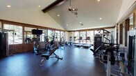 Located at 201 Deann Dr in Independence, Oregon, this fitness center is a well-appointed, single-floor facility designed to support a full range of workout routines. The space is defined by its striking vaulted ceiling with exposed dark wood beams, recessed lighting, and a ceiling fan that together create an open, airy atmosphere. Warm wood trim and wainscoting frame the interior walls, lending a rustic yet polished aesthetic throughout.

Large windows and glass-panel doors line the perimeter of the main workout area, allowing generous natural light to flood the floor and offering views of the surrounding greenery. The durable rubber flooring provides a safe, cushioned surface suitable for a variety of exercises.

The main workout floor is equipped with a comprehensive array of cardio machines, including treadmills, ellipticals, and stationary bikes, alongside cable crossover machines, weight benches, and selectorized strength equipment. A dedicated free weight area features a full rack of dumbbells and wall-mounted mirrors that enhance the sense of space. A secondary room houses additional strength machines and provides direct access to the outdoors. Near the entry, a water station and hand sanitizer dispenser are conveniently available. The fitness center is well-organized, functional, and thoughtfully designed for an effective workout experience.