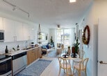 Located at 5375 NW Seventh St in Miami, FL, this single-floor residence offers a cohesive, modern design with a warm bohemian aesthetic throughout. The open-plan layout seamlessly connects the kitchen, dining, and living areas, creating an airy and functional flow. Large floor-to-ceiling windows at the far end of the living space flood the interior with natural light and provide direct access to a private balcony, offering outdoor views of the surrounding greenery.

The kitchen is well-appointed with a two-tone cabinetry design — glossy white upper cabinets paired with warm wood-grain lower cabinets — set against a white tile backsplash. A full suite of stainless steel appliances, including a side-by-side refrigerator with ice maker, electric range, built-in microwave, and dishwasher, ensures a fully functional cooking space. Light wood-style tile flooring runs consistently throughout the unit.

The dining area features an intimate round table setting, while the living room is anchored by a ceiling fan and sheer white curtains. The bedroom is bright and serene, benefiting from balcony access and a ceiling fan, with clean white walls that complement the space's relaxed character. The bathroom includes a floating wood-grain vanity, a large mirror, and light, neutral finishes.