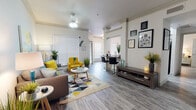 This single-floor residence offers a thoughtfully designed open-concept layout that seamlessly connects the living, dining, and kitchen areas. The living room is a welcoming space featuring crown molding, a ceiling fan, and wood-look flooring throughout. Large windows dressed with horizontal blinds allow ample natural light to fill the room, complementing the neutral color palette accented by bold yellow and teal décor touches.

Adjacent to the living area, a dedicated workspace nook provides a functional area with bar-style seating, making it ideal for remote work or study. The dining area features large windows that bring in natural light and offer outdoor views, creating a bright, airy setting for meals.

The kitchen is well-equipped with stainless steel appliances, including a gas range, microwave, and refrigerator. Gray shaker-style cabinetry pairs with dark countertops to deliver a contemporary aesthetic, while recessed lighting and wood-look flooring maintain a cohesive design throughout.

The bedroom is a spacious and serene retreat, featuring multiple windows for natural light and direct access to a well-organized walk-in closet. The bathroom is finished with gray cabinetry, dark countertops, a large vanity mirror, and matching wood-look flooring, maintaining the consistent modern style found throughout the entire residence.