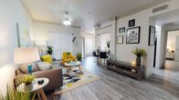 This single-floor residence offers a thoughtfully designed open-concept layout that seamlessly connects the living, dining, and kitchen areas. The living room is a welcoming space featuring crown molding, a ceiling fan, and wood-look flooring throughout. Large windows dressed with horizontal blinds allow ample natural light to fill the room, complementing the neutral color palette accented by bold yellow and teal décor touches.

Adjacent to the living area, a dedicated workspace nook provides a functional area with bar-style seating, making it ideal for remote work or study. The dining area features large windows that bring in natural light and offer outdoor views, creating a bright, airy setting for meals.

The kitchen is well-equipped with stainless steel appliances, including a gas range, microwave, and refrigerator. Gray shaker-style cabinetry pairs with dark countertops to deliver a contemporary aesthetic, while recessed lighting and wood-look flooring maintain a cohesive design throughout.

The bedroom is a spacious and serene retreat, featuring multiple windows for natural light and direct access to a well-organized walk-in closet. The bathroom is finished with gray cabinetry, dark countertops, a large vanity mirror, and matching wood-look flooring, maintaining the consistent modern style found throughout the entire residence.