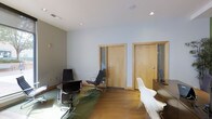 Located at 415-425 N Front St in Columbus, Ohio, this single-floor commercial space offers a well-appointed and modern work environment designed to support professional use. The interior showcases a clean, contemporary aesthetic characterized by smooth white and light gray walls, recessed ceiling lighting, and warm hardwood flooring that extends throughout the main area, contributing to a polished yet inviting atmosphere.

The open main area provides ample room for workstations and collaborative arrangements, as evidenced by the ergonomic task seating and mixed modern chairs arranged throughout the space. A glass-top desk and additional work surfaces add a sleek, functional quality to the layout.

Two interior doors with warm wood-toned frames lead to private enclosed offices or meeting rooms, each featuring sidelight glass panels that allow borrowed light to filter through while maintaining separation. The enclosed rooms appear to contain additional workstations, adding flexibility for private work or client-facing functions.

Ceiling-mounted speakers and recessed lighting ensure a comfortable acoustic and visual environment. The overall design balances open collaborative zones with private office areas, making this a versatile and professional space well-suited for a range of business uses.