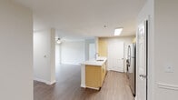 This single-floor residence offers a thoughtfully designed open-concept layout that seamlessly connects the kitchen, dining, and living areas. The kitchen serves as a functional centerpiece, featuring a peninsula island with a built-in sink, light wood cabinetry, white quartz-style countertops, and a classic white subway tile backsplash. Stainless steel appliances — including a four-burner gas range, over-the-range microwave, and refrigerator — complete the well-equipped cooking space. Warm hardwood-style flooring extends throughout the main living areas and kitchen, adding a cohesive and polished feel, while ceiling fans provide both style and comfort in multiple rooms. The living room is bright and open, with vertical blinds covering a sliding glass door that provides direct access to the outdoors and allows natural light to fill the space. The bedrooms are carpeted for added comfort and each feature ceiling fans and windows with outdoor views, creating a serene atmosphere. The bathroom includes a full-size soaking tub and shower combination with clean white tile surround and a curved chrome curtain rod. Throughout the residence, neutral tones, clean lines, and a bright, airy ambiance create a welcoming and move-in-ready environment.