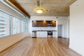 Located at 4501 Ford Ave in Alexandria, VA, this one-bedroom, two-bathroom loft-style residence offers a striking blend of industrial and contemporary design across a single floor. The open-concept living, dining, and kitchen area serves as the heart of the unit, characterized by soaring exposed concrete ceilings with visible ductwork and a ceiling fan, lending an urban, warehouse-inspired aesthetic. Wide-plank hardwood flooring flows throughout, complementing the clean white walls and modern finishes.

The kitchen is thoughtfully designed with a combination of rich dark wood upper cabinetry and white lower cabinets, grey countertops, a stainless steel dishwasher, range, and microwave. A wall of floor-to-ceiling windows floods the living and dining areas with abundant natural light and provides sweeping views of the surrounding treetops and Alexandria skyline.

The spacious primary bedroom continues the hardwood flooring and benefits from its own generous bank of windows, offering ample natural light and city views. The unit includes two closets, two full bathrooms, a dedicated laundry space with a stacked washer and dryer unit, and a utility room, providing practical everyday convenience throughout.