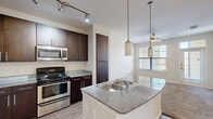 Located at 8011 Augusta Pines Dr in Spring, TX, this one-bedroom, one-bathroom residence offers a thoughtfully designed open-concept layout across a single floor. The living area features soft neutral carpeting and a ceiling fan, creating a comfortable and inviting atmosphere that flows seamlessly into the kitchen.

The kitchen is a functional highlight, showcasing rich dark-toned cabinetry that extends to the ceiling for ample storage, granite-look countertops, and a full suite of stainless steel appliances including a refrigerator, range, and microwave. A curved kitchen island with an integrated sink and pendant lighting above serves as both a prep space and a casual dining area. Track lighting and wood-look flooring complete the kitchen's contemporary aesthetic.

The bedroom is a well-proportioned retreat featuring plush carpeting, a ceiling fan, and a generously sized window that fills the room with natural light and offers pleasant outdoor views. An adjoining bathroom connects to a dedicated walk-in closet, providing practical storage. The bathroom features tile surround and hardwood-style flooring. Throughout the residence, neutral tones, clean lines, and modern fixtures create a cohesive and comfortable living environment.
