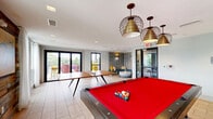 Located at 465 Memorial Dr SE in Atlanta, GA, this dynamic community amenity space is thoughtfully designed to offer a variety of social and recreational experiences across a single, well-appointed floor.

The interior game room is a lively gathering hub, featuring large windows that flood the space with natural light and frame treetop views. A ping-pong table takes center stage on light tile flooring, while a red felt billiards table anchors the back of the room beneath warm pendant lighting. Reclaimed wood wall accents and eclectic artwork add character and warmth to the contemporary layout.

Adjacent to the game room, a cozy lounge nook offers an intimate retreat with wraparound teal bench seating, colorful throw pillows, a sculptural round coffee table, and a striking textured accent wall illuminated by gold wall sconces—creating a warm, stylish atmosphere.

The space opens onto a covered outdoor terrace defined by bold red steel pergola beams and string lights overhead. Wicker lounge furniture in vibrant blue and coral tones is arranged around a concrete coffee table, all set against sweeping views of Atlanta's treetop skyline.

An outdoor dining area with warm wood-clad walls, a long communal table, bright yellow seating, and a mounted TV completes the space, offering a functional and inviting al fresco setting for gatherings.