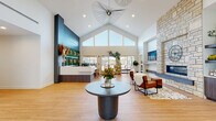 Located at 5302 S Champions Drive in Rogers, Arkansas, this single-story clubhouse is a thoughtfully designed community amenity facility offering a diverse range of spaces for work, fitness, and socializing. The building's centerpiece is a dramatic main lobby distinguished by soaring vaulted ceilings with clerestory windows that flood the space with natural light. A striking stone fireplace anchors one side of the room, while a bold teal accent wall frames the reception area. An eye-catching sculptural pendant light and light wood flooring complete the modern aesthetic.

Adjacent to the lobby, a fully equipped kitchen features floor-to-ceiling cabinetry in rich wood tones, stainless steel appliances, quartz countertops, and pendant lighting over a central island. The social lounge and game room offer pool and shuffleboard tables, large windows with outdoor views, and open space for gathering.

The fitness center is divided into two well-equipped zones: a cardio area with treadmills and mirrored walls, and a strength training zone with free weights, benches, cable machines, and exercise balls beneath vaulted ceilings. Dedicated coworking areas provide both collaborative conference-style seating and individual workstations with wall-mounted displays. A bright social dining room with round tables and large windows rounds out this versatile community space.