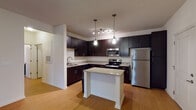 This single-floor residence at Spring House Apartments offers a thoughtfully designed layout with modern finishes and functional living spaces. The kitchen serves as a central highlight, showcasing rich dark cabinetry extending to the ceiling for ample storage, granite countertops, a central island with pendant lighting overhead, and a full suite of stainless steel appliances including a range, microwave, dishwasher, and refrigerator. Warm wood-style flooring runs throughout the kitchen and main living areas, contributing to a cohesive aesthetic.

The living area is generously proportioned, featuring a ceiling fan and French doors that open to the outdoors, allowing natural light to fill the space. A separate bedroom offers plush carpeting, a ceiling fan, and dual windows that bring in additional natural light and views of surrounding greenery.

The bathroom is appointed with dark cabinetry and granite countertops, complementing the kitchen's design language, with tiled accents adding a refined touch. A dedicated in-unit laundry room provides added convenience, housing a full-size washer and dryer on durable wood-style flooring. Overall, the residence presents a clean, contemporary ambiance with consistent finishes throughout.