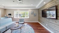 Located at 20 Harbor Village Drive in Middletown, Rhode Island, this single-story community clubhouse serves as the central gathering hub for Harbor Village residents. The space is thoughtfully designed with a coastal-inspired aesthetic, combining warm hardwood flooring, recessed lighting, and a neutral color palette throughout.

Upon entry, a welcoming reception lounge greets visitors with a "Welcome to Harbor Village" sign, a beverage cooler, and light blue upholstered seating arranged around a large window overlooking the greenery outside. The open layout transitions seamlessly into a spacious lounge and entertainment area, highlighted by a striking full-wall shiplap wood accent panel housing a wall-mounted flat-screen television. A second TV is visible in an adjoining nook, offering additional viewing areas. Natural light pours in through multiple windows, and a tray ceiling detail adds architectural character to the main gathering space.

The facility also includes a dedicated on-site laundry room equipped with a full row of modern LG front-load washers and dryers finished in sleek metallic tones. Warm wood flooring continues here, and a window provides natural light, making the space functional yet pleasant. Together, these amenities offer residents a comfortable, well-appointed community environment.