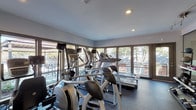 The fitness center at Summit in Lexington, Kentucky offers a well-equipped, single-floor facility designed to support a comprehensive workout experience. The space is thoughtfully laid out to accommodate a wide range of exercise needs, from cardiovascular training to strength and resistance work.

Large, floor-to-ceiling windows line the perimeter of the cardio zone, flooding the area with natural light and providing pleasant outdoor views of the surrounding landscape. This section houses multiple treadmills and elliptical machines, creating an airy and motivating environment for aerobic exercise.

A glass-partitioned area separates the free weights section, which features a full rack of dumbbells and a weight bench, providing an organized and dedicated space for targeted strength training. The use of glass walls maintains an open, connected feel throughout the facility.

The strength equipment zone is anchored by a multi-station cable machine with various attachments, complemented by benches and additional resistance apparatus. Full-length mirrors line one wall, enhancing the sense of space and allowing users to monitor their form.

Throughout the facility, durable rubber flooring provides both safety and comfort. Recessed lighting supplements the abundant natural light, ensuring the space remains well-lit at all hours. Fitness center rules are posted near the entrance, reflecting a structured and professional environment.