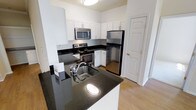 This single-floor residence offers a thoughtfully designed living space with a strong emphasis on modern finishes and functional layout. The kitchen serves as a central highlight, showcasing sleek dark granite countertops that provide a striking contrast against the bright white cabinetry. A peninsula with an integrated stainless steel sink adds both workspace and a natural division between the kitchen and adjacent areas, making it ideal for both cooking and casual entertaining. The kitchen is fully equipped with stainless steel appliances, including a refrigerator, electric range, and over-the-range microwave, all contributing to a cohesive, contemporary aesthetic. White shaker-style upper and lower cabinets offer generous storage throughout. Light hardwood-style flooring runs through the space, enhancing the sense of openness and warmth. The crisp white walls and flush ceiling lighting keep the interior feeling bright and clean. A paneled interior door provides access to an additional room or storage space, adding to the overall practicality of the layout. The combination of dark countertops, white cabinetry, and stainless steel fixtures creates a timeless, polished look throughout this well-maintained residence.