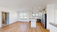 Located at 208 Windfall Way in Myrtle Beach, SC, this two-story home offers a well-designed layout spread across two floors. The main level hosts the majority of the living space, featuring an open-concept kitchen and living room that serves as the heart of the home. The kitchen is outfitted with stainless steel appliances—including a refrigerator, range with a wall-mounted hood vent, dishwasher, and microwave—complemented by quartz countertops, white upper cabinetry, gray lower cabinetry, a subway tile backsplash, and a central island. Light hardwood-style flooring runs throughout the main living areas, contributing to a bright, cohesive aesthetic. A set of French doors with a transom window opens to a small balcony, filling the living room with natural light. The shared bathroom features a dual-sink vanity with blue-gray cabinetry, a large framed mirror, and modern light fixtures. Both bedrooms are carpeted and receive ample natural light through double windows, each equipped with ceiling fans. The primary bedroom is generously sized with dedicated closet space. A small entry vestibule on the ground level leads upstairs, connecting all areas through well-placed hallways.