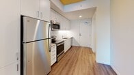 Located at 1090 NE 91st Ave in Hillsboro, Oregon, this single-floor unit offers a thoughtfully designed layout with modern finishes throughout. The kitchen is a standout feature, showcasing a full suite of stainless steel appliances including a refrigerator, electric range, over-the-range microwave, and dishwasher. Crisp white cabinetry extends floor to ceiling, providing generous storage, while a white subway tile backsplash and clean countertops complete the contemporary aesthetic. Warm wood-look luxury vinyl plank flooring runs throughout the unit, adding a welcoming contrast to the bright white walls. A distinctive natural wood-paneled ceiling adds warmth and architectural character to the kitchen and living areas. The bedroom is generously sized, featuring the same wood-paneled ceiling, a ceiling fan with light fixture, and a window that brings in natural light with views of the surrounding greenery. A walk-in closet with built-in shelving provides excellent organization and storage space. The bathroom is finished in a neutral palette with a single-sink vanity, wall-mounted storage cabinet, a large mirror, and durable wood-look flooring. Accessibility-friendly grab bars are thoughtfully incorporated. The unit's clean, modern design and functional layout make it a comfortable and practical living space.
