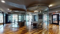 Located at Northpoint Crossing in College Station, TX, this single-floor amenity space delivers a sophisticated and modern environment defined by bold architectural choices. The most distinctive feature is the use of curved, floor-to-ceiling glass partitions that create semi-enclosed circular meeting and lounge areas within the open floor plan. These transparent enclosures allow light to flow freely throughout the space while providing a sense of defined purpose and privacy within each zone.

Rich, multi-toned hardwood flooring extends across the entire space, adding warmth and a natural contrast to the sleek glass and metal architectural elements. Each glass-enclosed area is furnished with round tables and contemporary seating, making them well-suited for meetings, study sessions, or social gatherings. Recessed lighting and stylish pendant fixtures overhead illuminate the space with both ambient and accent light.

Along the perimeter, large windows and glass-fronted walls invite abundant natural light and views of the surrounding outdoor areas. Decorative wall art, including bicycle wheel-inspired metalwork panels, adds an urban, creative character to the interior. The open corridor areas connecting each zone provide a clean, navigable layout. Overall, this amenity space combines functional design with a contemporary aesthetic, offering an engaging and versatile environment for its users.