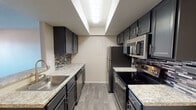 This single-floor residence offers a thoughtfully designed layout that balances functionality and comfort throughout. The galley-style kitchen is a standout feature, showcasing dark cabinetry with brushed nickel hardware, light granite-style countertops, a mosaic tile backsplash, and a full suite of stainless steel appliances including a refrigerator, electric range, dishwasher, and over-the-range microwave. Light wood-look flooring runs underfoot, and recessed overhead lighting illuminates the space efficiently.

A pass-through window connects the kitchen to the living area, creating an open, communicative flow between spaces. The living room is carpeted and features a fireplace, a textured ceiling, and sliding glass doors that open to a private patio, allowing natural light to fill the room. A ceiling fan is visible in the adjoining hallway or dining area, adding to the home's practical amenities.

The bedroom is generously sized with plush carpeting, a textured ceiling, and a window with blinds offering views to the surrounding area. The bathroom is clean and functional, featuring wood-look flooring, a shower-tub combo, and neutral wall tones. An in-unit laundry area with a washer and dryer rounds out the home's convenient and self-sufficient layout.
