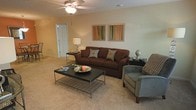 Located at 2640 Latrobe Avenue in Fayetteville, North Carolina, this single-story home offers a comfortable and functional layout designed for everyday living. The living area serves as the heart of the home, showcasing a warm, neutral color palette with soft carpeted flooring that adds a cozy feel underfoot. A ceiling fan with a light fixture anchors the room from above, providing both comfort and illumination. The space is generously sized, offering ample room for seating and relaxation. Walls are finished in a clean, light tone that enhances the open and airy atmosphere of the room. Tasteful wall art in complementary colors adds a decorative touch, contributing to the inviting character of the space. An interior door provides access to additional areas of the home, suggesting a thoughtful and connected floor plan. Overall, this single-floor residence presents a straightforward, livable layout with a calm and neutral aesthetic that offers a solid foundation for personalization and comfortable day-to-day living in the Fayetteville community.