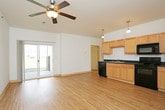 This single-story unit offers a clean, modern layout designed for comfortable everyday living. The open-concept main living area seamlessly connects to the kitchen, which is equipped with light maple cabinetry, dark countertops, and a full suite of black appliances including a range, microwave, dishwasher, and refrigerator. Pendant lighting illuminates the kitchen, while a ceiling fan and sliding glass door leading to a patio enhance the living space with natural light and outdoor access. Warm-toned hardwood-style flooring runs throughout the entire unit, creating a cohesive and inviting atmosphere. Each bedroom is generously sized, featuring ceiling fans, large windows that bring in natural light, and built-in closets for ample storage. One bedroom includes an en-suite bathroom. The unit offers multiple bathrooms, each finished with light maple vanities, white fixtures, and either a walk-in shower or a shower-tub combination. Clean white walls and neutral trim throughout contribute to a bright, airy feel that makes the space feel open and move-in ready. The overall design prioritizes functionality and comfort, with a consistent aesthetic across all rooms.