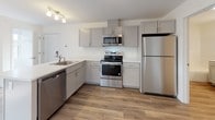 Located at 3 Carriage Walk Way in Scarborough, Maine, this single-floor unit offers a clean, modern design with a bright and open layout. The living area is generously proportioned, featuring durable wood-style flooring that extends throughout the main living spaces. Natural light streams in through multiple windows fitted with blinds, and a door provides direct access to an outdoor balcony. A wall-mounted mini-split unit ensures year-round climate comfort, complemented by baseboard heating along the perimeter walls.

The kitchen is thoughtfully designed with grey shaker-style cabinetry, light quartz countertops, and a peninsula that creates a natural division between the kitchen and living area. A full suite of stainless steel appliances — including a refrigerator, electric range, built-in microwave, and dishwasher — adds both functionality and a polished aesthetic. Track lighting above the kitchen provides focused illumination.

The bedroom is carpeted for comfort and features a spacious reach-in closet with double doors. Crisp white walls and a neutral palette carry throughout the space, lending a clean and cohesive feel. The full bathroom is well-appointed with wood-style flooring, a white vanity with quartz countertop, brushed nickel fixtures, a large mirror, and a full soaking tub with shower.