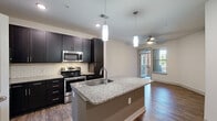 Located at 6010 Attleboro Dr in Cary, NC, this well-appointed one-bedroom, one-bathroom residence offers a thoughtfully designed single-level layout. The open-concept kitchen serves as the heart of the home, showcasing rich dark cabinetry, a classic subway tile backsplash, stainless steel appliances, and a generous granite-topped island with an undermount sink and pendant lighting overhead. The kitchen flows seamlessly into the dining area and living space, which is brightened by a ceiling fan and a glass door leading to a private balcony with outdoor views. Hardwood-style flooring runs consistently throughout the main living areas, enhancing the cohesive aesthetic. The bedroom is a comfortable retreat featuring a ceiling fan, a window with natural light, and direct access to a walk-in closet outfitted with multi-tier wire shelving for ample storage. The bathroom is finished with a frameless glass walk-in shower accented by a decorative teal tile border, white tile surround, and polished chrome fixtures. Clean white walls, neutral tones, and consistent finishes throughout contribute to a modern, move-in-ready ambiance ideal for those seeking a functional and stylish home in the Cary, NC area.