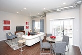 This single-floor residence combines modern design with industrial-inspired elements throughout its well-appointed layout. Exposed metallic ductwork runs prominently across the ceilings, adding an urban loft aesthetic to the otherwise clean, neutral interior palette.

The kitchen is outfitted with white cabinetry, stone-finish countertops, and a full suite of black appliances, including a refrigerator, range, and microwave. A peninsula with seating provides additional prep space and casual dining. Dark hardwood-style flooring anchors the kitchen and extends into the living area.

The living room offers generous space, with recessed lighting, large windows allowing natural light, and views of the surrounding area. An adjacent dining nook completes the open-feeling common area.

The bedroom features plush carpeting, tall ceilings with continued ductwork detail, and a window with exterior views. A walk-in closet fitted with white wire shelving and hanging rods provides ample organized storage.

The bathroom includes a stone-finish vanity countertop, white cabinetry, hardwood-style flooring, and a shower-tub combination. A dedicated laundry area houses a full-size washer and dryer with wire shelving above for additional storage.