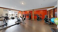 Located at 1005 Gramsie Rd in Shoreview, Minnesota, this generously sized fitness center offers a comprehensive workout environment designed to inspire and motivate. The space is thoughtfully divided into distinct functional zones, each catering to different training needs.

The cardio area is anchored by floor-to-ceiling windows that flood the room with natural light and provide open views of the surrounding outdoor space, creating an energizing atmosphere. Treadmills, ellipticals, stair climbers, rowing machines, and stationary bikes are positioned to take full advantage of this bright, airy setting.

The strength training zone is equally impressive, featuring a full power rack, a dumbbell rack with a wide weight range, adjustable benches, cable machines, and a wall of mirrors that amplify the sense of space. Rubber flooring throughout ensures safety and durability across all workout areas.

Architectural details include warm wooden beam accents, exposed ductwork, and a striking wood-paneled ceiling in the cardio section that adds a refined, contemporary character. Bold motivational phrases — "Smashing Goals," "Walk In Strong," and "Doing Work" — are emblazoned across the vibrant orange and navy accent walls, reinforcing the space's energetic identity.

Recessed lighting complements the abundant natural light, ensuring the entire facility is well-lit at all hours. This fitness center is a well-appointed, full-service exercise facility built for serious training.