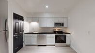 Located at 7008 Erie Rd in Derby, NY, this thoughtfully designed single-floor unit offers a clean, modern aesthetic throughout its efficiently arranged layout. The open-concept kitchen and living area serves as the heart of the unit, featuring a sleek galley-style kitchen outfitted with stainless steel appliances — including a dishwasher, electric range, and over-the-range microwave — complemented by white shaker cabinetry, dark countertops, and a classic subway tile backsplash. Light-toned hardwood-style flooring extends seamlessly through the living space, enhancing the bright, airy feel created by recessed lighting and crisp white walls.

The bedroom offers a comfortable, private retreat with a window overlooking greenery, continuing the same light flooring and neutral palette. A set of bold, dark double doors provides access to a closet, adding a striking design contrast to the room's otherwise soft tones.

The bathroom is neatly finished with a tiled tub-and-shower combination featuring chrome fixtures, a gray vanity with a white basin, and a large mirror framed by modern lighting. Throughout the unit, clean lines and a consistent neutral color scheme create a cohesive, contemporary atmosphere that is both functional and inviting.