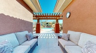 Located at 80175 Avenue 52 in La Quinta, California, this two-story property showcases a striking Southwestern architectural design characterized by warm terracotta and bold yellow-and-orange stucco exteriors, clay tile roofing, and rich earthy tones throughout. The standout feature of the community is its expansive resort-style outdoor area, centered around a large, shimmering swimming pool with crystal-clear turquoise water. The pool deck is generously appointed with rows of red cushioned lounge chairs, striped orange-and-yellow cabanas, and vibrant potted bougainvillea and desert plantings that add vivid color to the surroundings. Soaring palm trees frame the space, providing both shade and a distinctly desert-resort ambiance under the brilliant Southern California sky. A covered pergola lounge area, supported by bold terracotta-colored columns, offers a shaded retreat with comfortable wicker seating — ideal for relaxing while overlooking the pool. An outdoor grill station is also available on the pool deck, enhancing the space's suitability for outdoor entertaining. The combination of colorful architecture, manicured landscaping, and well-appointed amenities creates an inviting, resort-quality outdoor environment reflective of the Coachella Valley lifestyle.