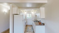 Located at 5125 SW Scholls Ferry Rd in Portland, Oregon, this two-bedroom, one-bathroom unit offers a practical and well-organized single-floor layout. The living room greets you with a distinctive exposed beam ceiling, a ceiling fan with light fixture, and tile flooring that extends into the hallways. A large window at the far end of the living area allows natural light to fill the space with a bright, open feel.

The galley-style kitchen is efficiently designed with white cabinetry lining both walls, offering generous storage. Stone-toned countertops, a stainless steel sink, and a window overlooking the outdoors complete the functional setup, which also accommodates a full-size refrigerator and range.

Both bedrooms feature soft carpet flooring and exposed ceiling beams consistent with the rest of the home. The primary bedroom includes a sliding-door closet with a built-in rod for ample storage. The second bedroom benefits from a large window with views of the surrounding greenery and receives plentiful natural light. Baseboard heaters provide warmth in the bedrooms.

The bathroom is clean and straightforward, featuring a tub-shower combo, a white vanity with under-cabinet storage, and tile flooring. Throughout the unit, a neutral color palette and consistent design elements create a cohesive, functional living environment.