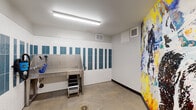 This single-level underground facility offers a comprehensive range of amenities designed to support everyday convenience. The parking area is expansive, constructed with exposed concrete ceilings, columns, and masonry walls that give the space a solid, utilitarian character. Clearly marked, numbered stalls accommodate a substantial number of vehicles, with designated accessible parking spaces near building entry points. EV charging stations are installed along the walls, reflecting a forward-thinking approach to resident needs. Overhead fluorescent strip lighting ensures consistent illumination throughout the garage.

Bicycle storage is integrated directly into the parking area, with wall-mounted bike racks positioned between stalls for efficient use of space. A secured chain-link storage enclosure provides additional locked storage capacity for residents. Building access is conveniently available via interior doors connecting directly to the elevator and corridor areas.

A dedicated pet wash station adds a practical and distinctive amenity to the level. This room features a stainless steel grooming tub with a handheld sprayer, a non-slip step stool, floor drainage, and a striking accent wall of blue and white vertical tiles. A bold, colorful abstract mural animates one wall, lending an unexpected artistic touch to an otherwise functional space.