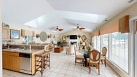Located at 101 Old Oak Ln in Colonial Heights, VA, this single-floor space offers an open, flowing layout that seamlessly connects the living room, dining area, and kitchen. The living room is a standout, boasting vaulted ceilings accentuated by a skylight and a decorative ceiling fan, a tile-surround fireplace, and light tile flooring throughout. The airy, warm-toned walls and generous recessed lighting contribute to a welcoming ambiance. The dining area is bathed in natural light from a large picture window and a glass-panel door, both offering direct views of an outdoor pool area. Warm valance treatments frame the windows, adding a refined touch. The kitchen is efficiently designed with light wood cabinetry, granite countertops, stainless steel appliances, and a spacious peninsula bar fitted with seating for multiple guests — ideal for casual dining or entertaining. Vaulted ceilings continue into this area, enhancing the sense of openness. Throughout the space, consistent tile flooring, neutral tones, and abundant natural light create a cohesive, comfortable atmosphere. The direct pool access via the dining area door further extends the living experience to the outdoors.