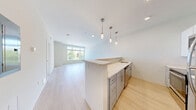 Located at 300 N Main St in Mansfield, Massachusetts, this one-bedroom, one-bathroom residence offers a thoughtfully designed floor plan that maximizes every square foot of its single-level layout. Light-toned hardwood-style flooring runs throughout the main living areas, lending a clean, contemporary aesthetic to the space.

The open-concept kitchen and living room serve as the heart of the home. The kitchen features a peninsula with pendant lighting overhead, stainless steel appliances including a full-size refrigerator, stove, and microwave, white cabinetry, and light countertops. The adjoining living area is bright and airy, with large windows that invite abundant natural light and frame views of the surrounding greenery.

The bedroom is carpeted for comfort and benefits from a generous corner window arrangement, offering pleasant outdoor views. A dedicated in-unit laundry closet with a stacked washer and dryer adds everyday convenience. Two additional closets provide ample storage throughout the unit.

The bathroom is clean and functional, featuring a full tub-shower combination, a vanity with light countertops, and modern fixtures with a neutral color palette that complements the rest of the home. A utility room rounds out the practical amenities of this well-appointed residence.