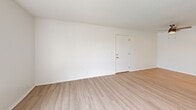 This single-story, 2-bedroom, 1-bathroom residence offers a clean and functional layout across a well-proportioned floor plan. The combined kitchen and living room area forms the heart of the unit. The living room features light wood-style vinyl flooring, bright white walls, a textured ceiling, and a large sliding glass door that fills the space with natural light and provides outdoor views. A separate entry door leads directly into this open area. The galley-style kitchen is efficiently designed with white cabinetry lining both walls, light countertops, a built-in sink, and full-size white appliances including a refrigerator and stove, all beneath a flush ceiling light. A hallway connects the main living area to the private sleeping quarters. Both bedrooms are carpeted in a neutral tan tone and feature white walls, textured ceilings, and windows with vertical blinds that allow natural light. The primary bedroom includes a dedicated closet with built-in shelving. The second bedroom also benefits from a closet. The full bathroom features a white tub-shower combination with built-in shelving and a curtain rod. Two closets provide additional storage throughout the unit, maintaining a tidy and organized living environment overall.